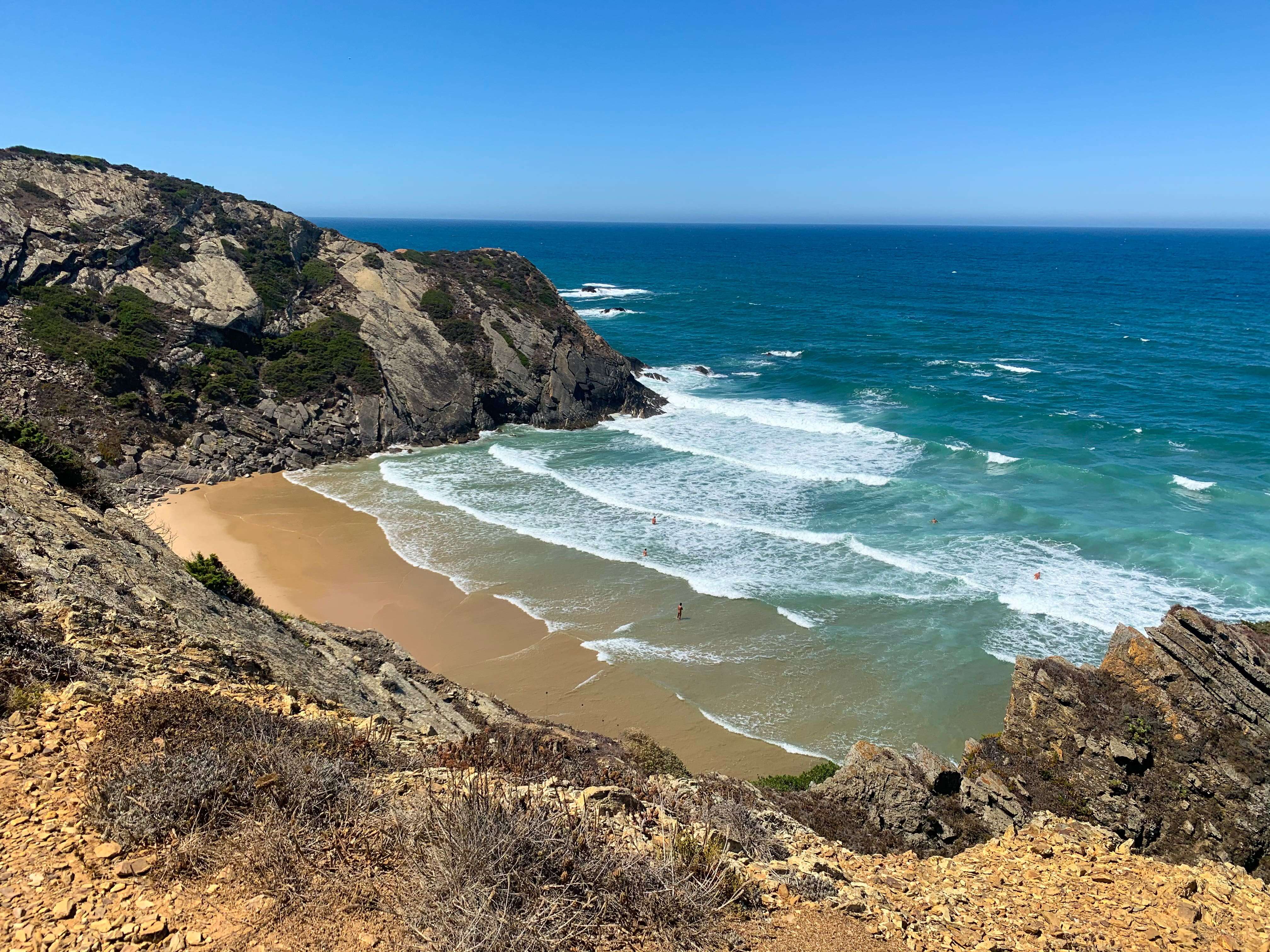 Discover a scenic view at this small, secluded beach in Sagres, where rocky cliffs cradle the sandy shore. The turquoise waves gently lap under a clear sky as sparse vegetation adorns the cliffs, inviting you to explore the hidden gems of things to do in Sagres.