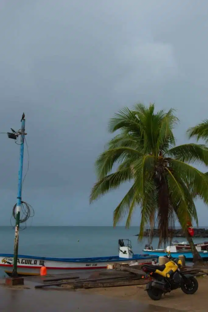 Boats docked along the waterfront in Bluefields, Nicaragua, under stormy skies, with a yellow motorcycle and palm trees in view — a common starting point for getting to the Corn Islands. Bluefields is one of the key launch locations when planning how to get to Corn Island by ferry.