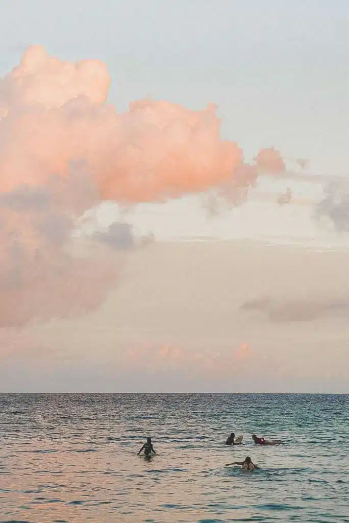Four people on surfboards float on calm ocean water under a sky with soft pink clouds during sunset—a serene scene and one of the top things to do in Hiriketiya.