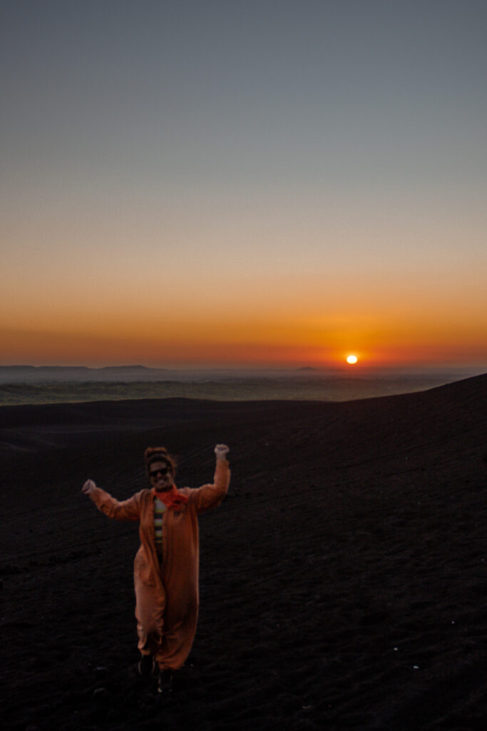 A person in an orange costume stands on dark, rocky terrain at sunset—perfect inspiration for your 10-Day Nicaragua Itinerary—as the sun dips low and the sky fades from orange to blue.