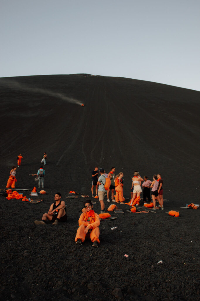 A group of people in orange suits relax on dark volcanic ash at the base of a steep slope—an adventurous stop perfect for any 10-Day Nicaragua Itinerary, with scattered gear and some members climbing or descending the hill behind them.