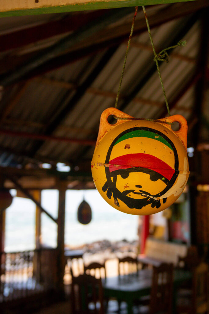 A yellow buoy painted with a stylized face wearing a red, yellow, and green hat hangs by a green string inside a rustic wooden structure—a charming spot you might discover on your 10-Day Nicaragua Itinerary. Tables and chairs sit in the background.