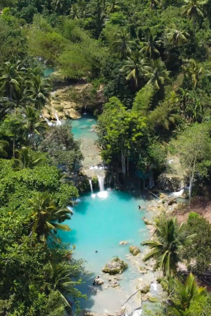 Aerial view of a turquoise blue river with small waterfalls surrounded by dense green tropical trees, perfect for any Philippines island-hopping itinerary.