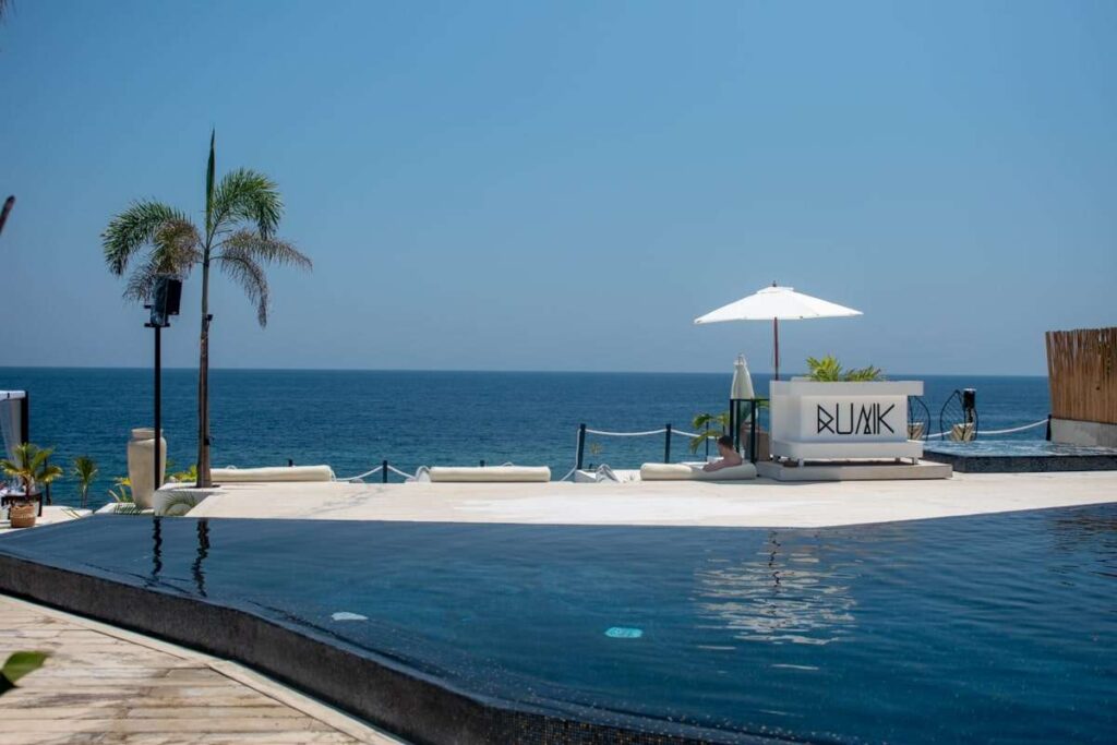Infinity pool overlooking the ocean with a white lounge area, palm trees, and a white umbrella under a clear blue sky—perfect for unwinding during your Philippines island-hopping itinerary.