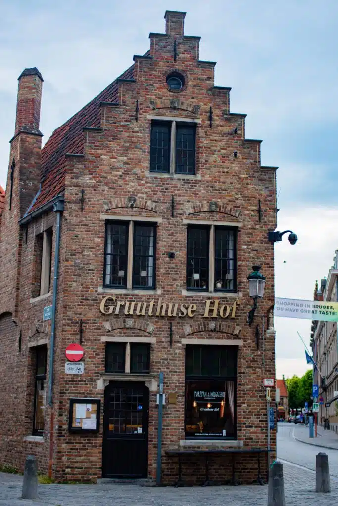 A historic brick building with a stepped gable roof houses the Gruuthuse Hof restaurant in Bruges, Belgium. The facade features large windows, a wooden door, and a "Gruuthuse Hof" sign above the entrance.