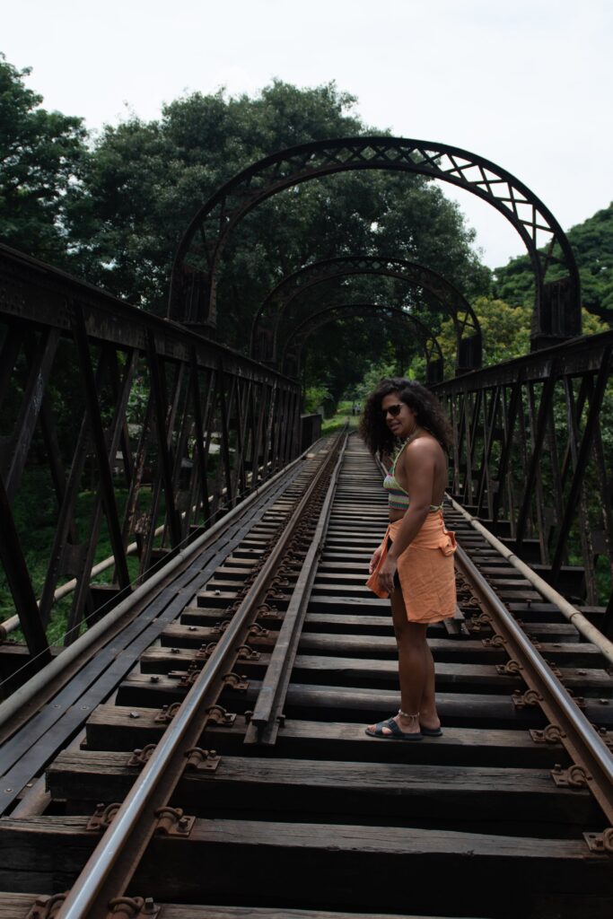 A woman stands on a metal railway bridge surrounded by trees, looking over her shoulderโembodying the spirit of solo adventure and inspiring the question: Is Sri Lanka safe for solo female travellers? The bridge has an arched structure overhead.