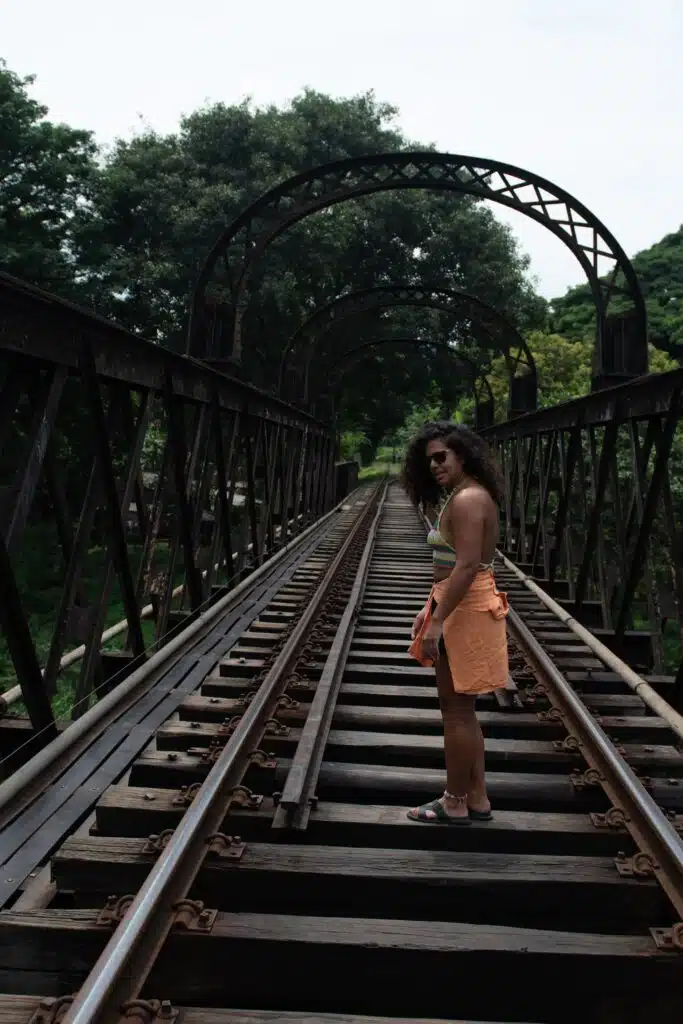 A woman stands on a metal railway bridge surrounded by trees, looking over her shoulder—embodying the spirit of solo adventure and inspiring the question: Is Sri Lanka safe for solo female travellers? The bridge has an arched structure overhead.