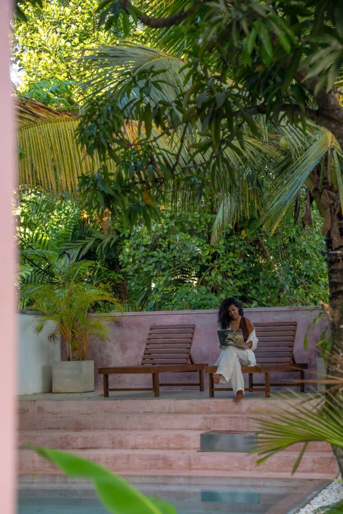 A woman sits on a wooden lounge chair by a pool, working on a laptop, surrounded by lush tropical plants in Sri Lankaโa serene setting that inspires confidence about whether Sri Lanka is safe for solo female travellers.