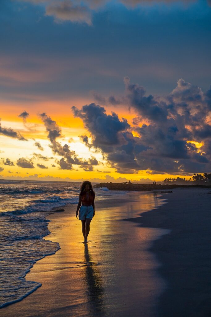 A person walks along the shoreline at sunset, dramatic clouds overhead and vibrant orange hues reflecting on wet sandโcapturing a tranquil moment that prompts you to wonder: Is Sri Lanka safe for solo female travellers?.