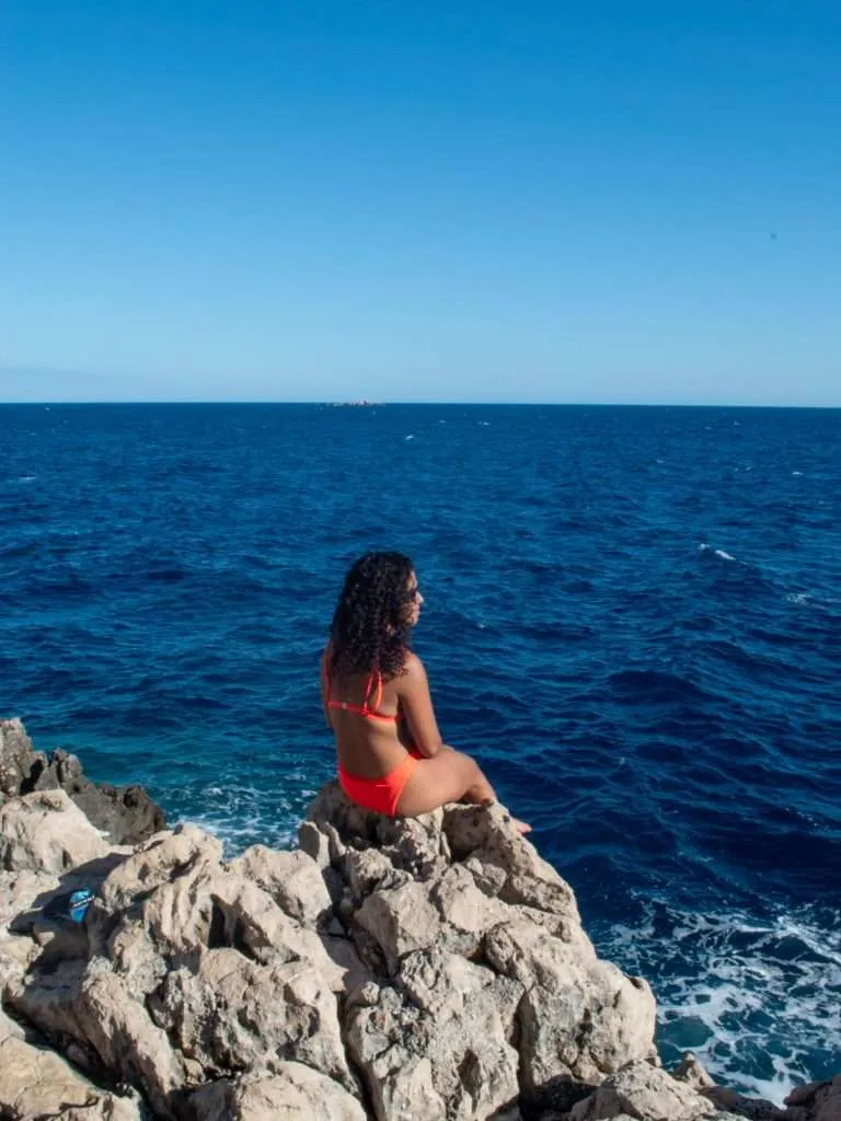 Woman sitting on a rock in Croatia overlooking the sea - What to pack for a trip to Europe
