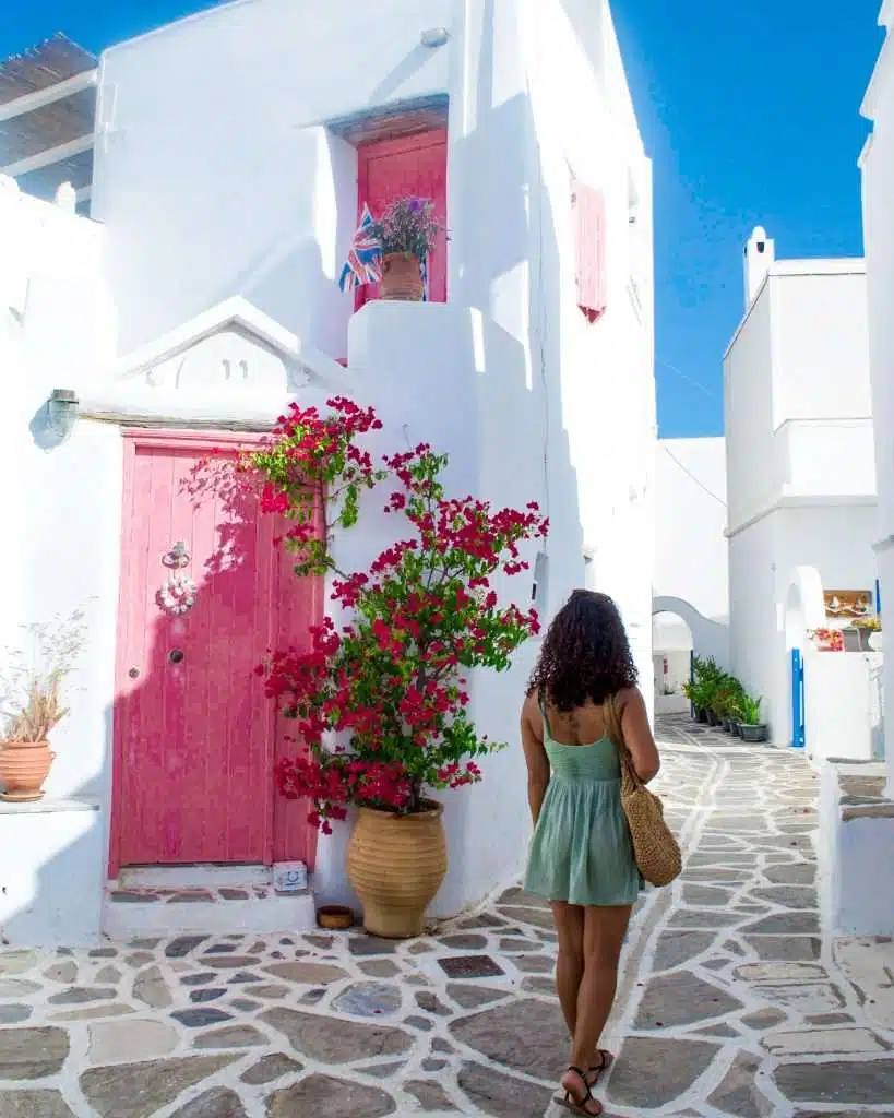 What to pack for a trip to Europe - Woman walking through cobbled streets of Greece past a bright pink door. 