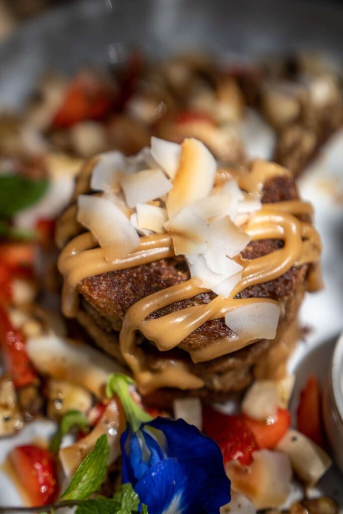 A close-up of a dessert topped with coconut flakes and caramel sauce, surrounded by chopped strawberries, nuts, and a blue edible flower—a sweet treat you might discover among the many things to do in Arugam Bay.