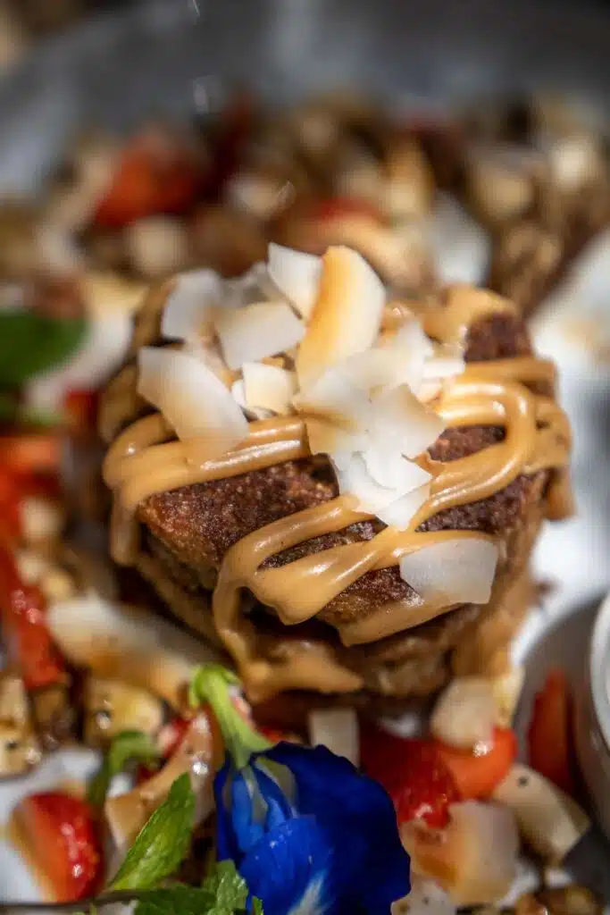 A close-up of a dessert topped with coconut flakes and caramel sauce, surrounded by chopped strawberries, nuts, and a blue edible flower—a sweet treat you might discover among the many things to do in Arugam Bay.