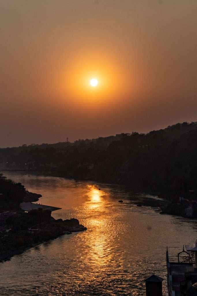 A serene sunset over a calm river, casting an orange glow across the water - Rishikesh India - Om Shanti Shanti Cafe