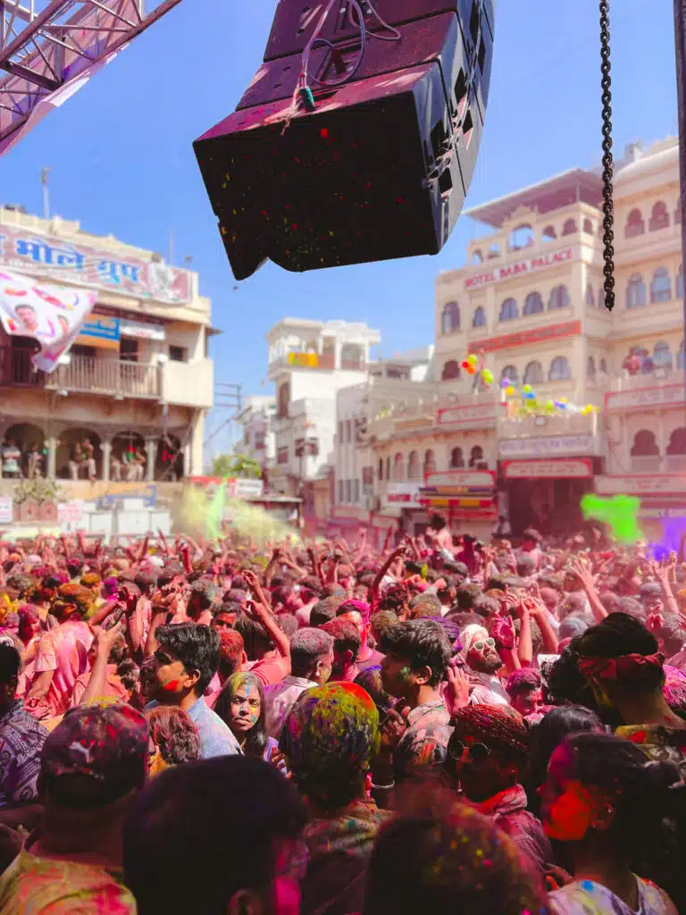 A large crowd celebrates Holi outdoors, throwing colorful powder in the air. People’s faces and clothes are covered in vibrant colors—a lively scene that highlights the spirit of India. Is India Safe For Solo Female Travellers? Events like this showcase its vibrant culture.