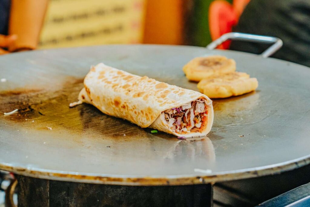 A close-up of a freshly made stuffed wrap and two small round breads cooking on a large, flat metal griddle—an inviting sight you might encounter during your 2-Day Pushkar Itinerary, with the wrap brimming with colorful vegetables.