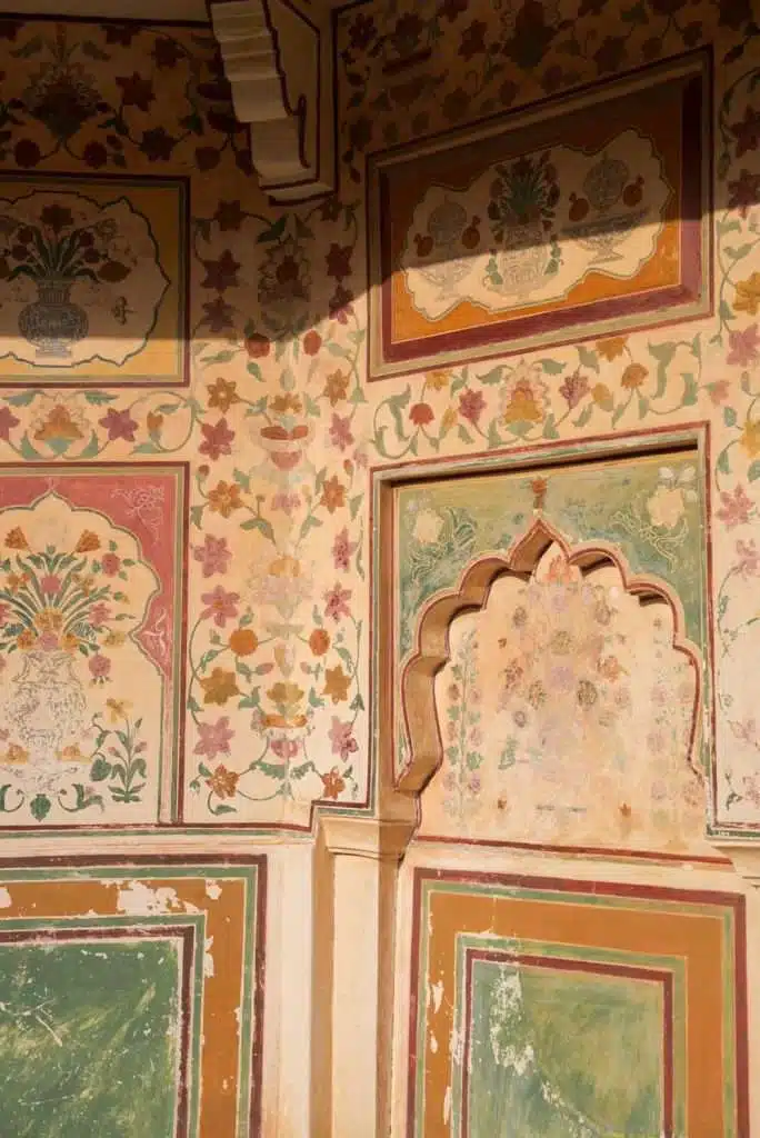 Sunlit corner of a wall with intricate floral and vase motifs in faded pastel colors, featuring an ornate arched niche—an exquisite highlight on a 2-Week North India Itinerary exploring traditional Indian architectural design.