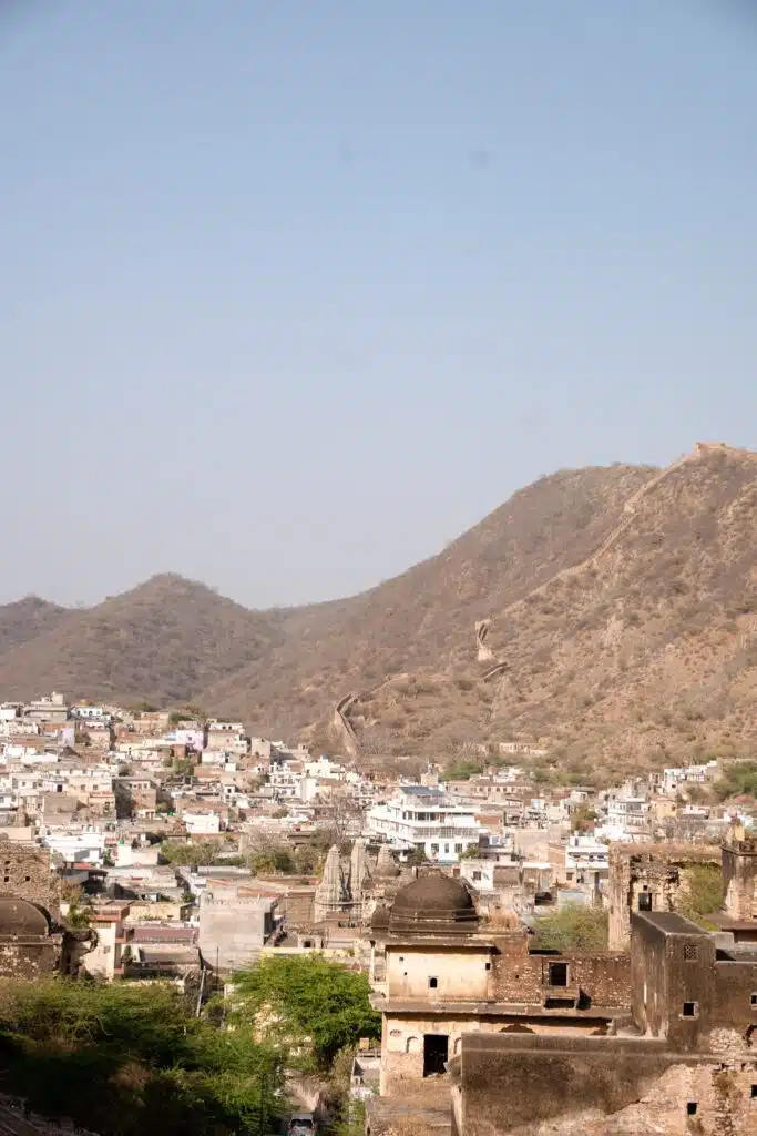 Backpacking India A view of an old city with densely packed buildings, set against brown, arid hills under a clear blue sky. Perfect for your 2-Week North India Itinerary, a stone wall winds along the ridge of the hills in the background.