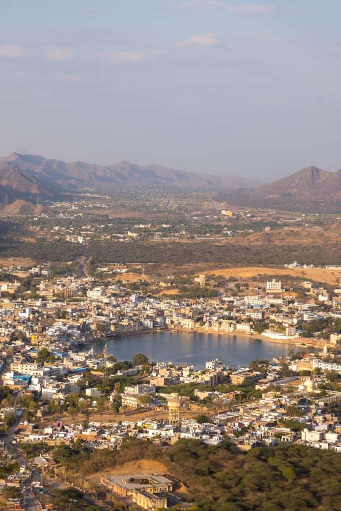 Aerial view of a city with white buildings surrounding a lake, set in a valley with dry hills and distant mountains—an iconic scene perfect for your 2-Week North India Itinerary under a partly cloudy sky.