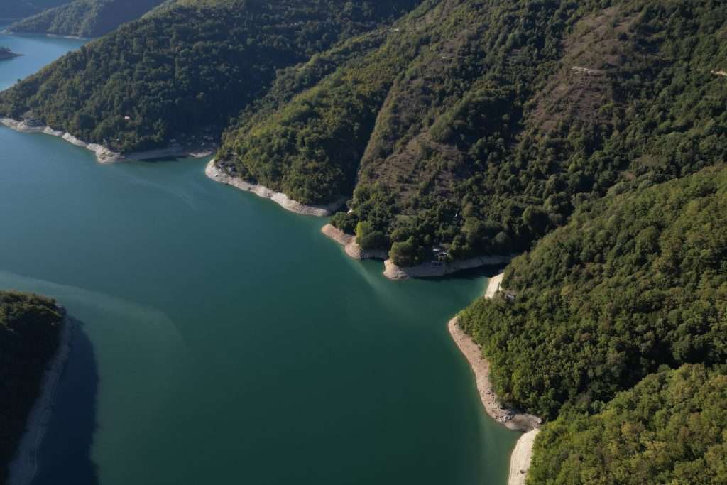 Aerial view of the Neretva River in Jablanica Bosnia and Herzegovina, surrounded by lush, green forested hills. The calm water contrasts with the dense vegetation on the steep slopes. A narrow shoreline is visible where the water meets the land, capturing the serene beauty experienced over 3 days here.