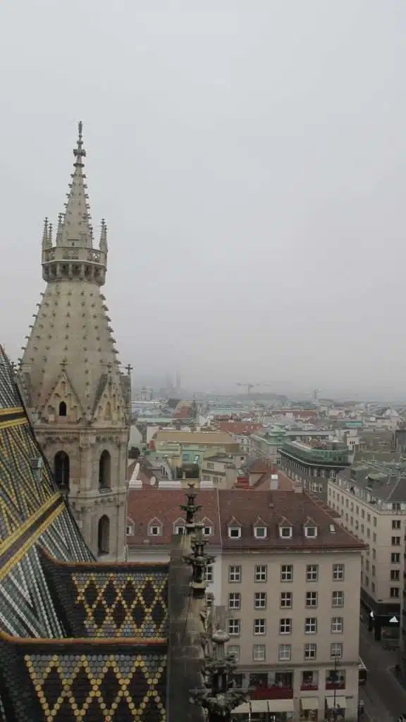 Discover this moody cityscape on a foggy day, featuring a Gothic-style cathedral tower rising above colorful tiled rooftops. As mist rolls over this picturesque landscape, it sets the perfect tone for your 1-week Eastern Europe itinerary, adding an atmospheric touch to your journey.