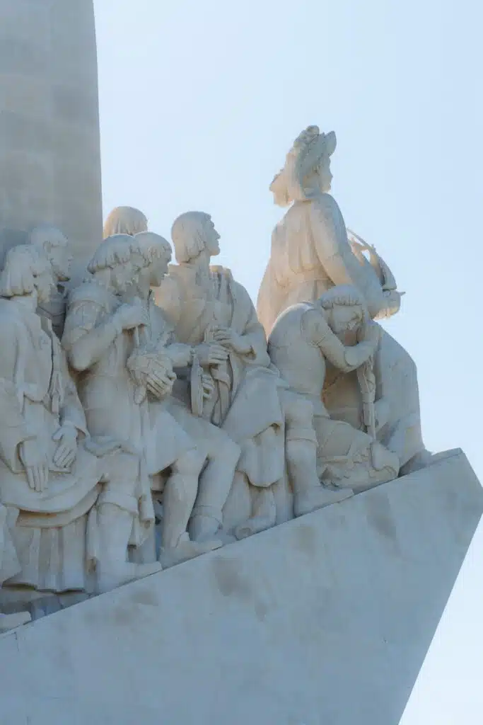 Stone statues of historical figures stand together on a monument in Lisbon, facing forward with one figure kneeling and holding a navigational instrument—a striking tribute you can discover during your 3 days in Lisbon.