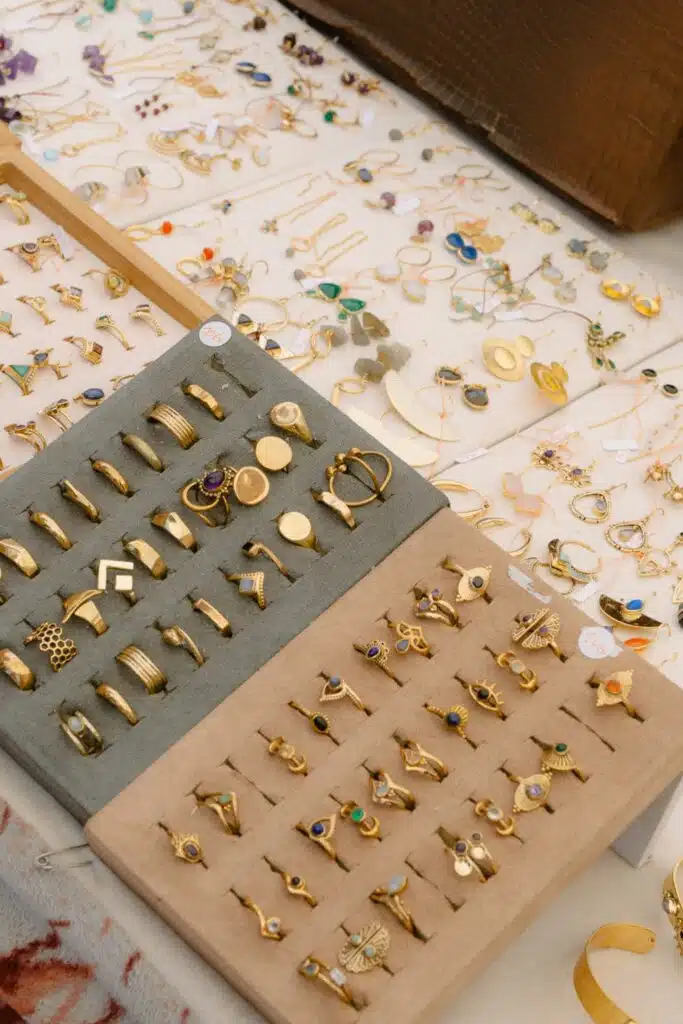 A display of assorted gold rings with various designs and gemstones on two cushioned trays—perfect for those spending 3 days in Lisbon, looking to find unique jewelry among earrings and necklaces arranged on a table in the background.