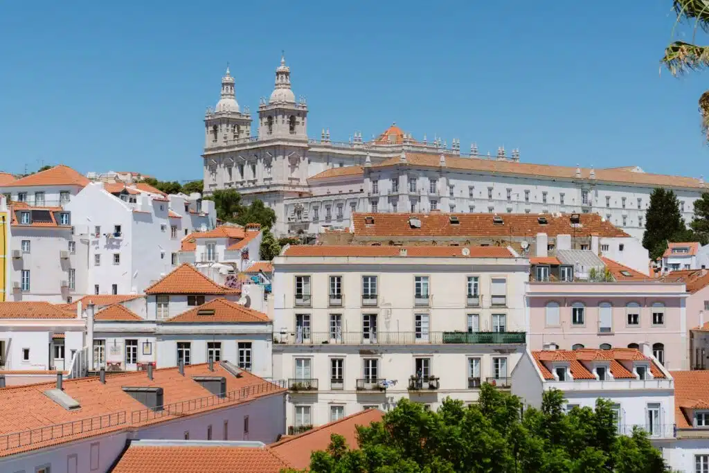 Cityscape of Lisbon, Portugal, with white and pastel buildings topped with red-tiled roofs. Perfect for exploring during 3 days in Lisbon, the São Vicente de Fora Church and Monastery stands out under a clear blue sky.