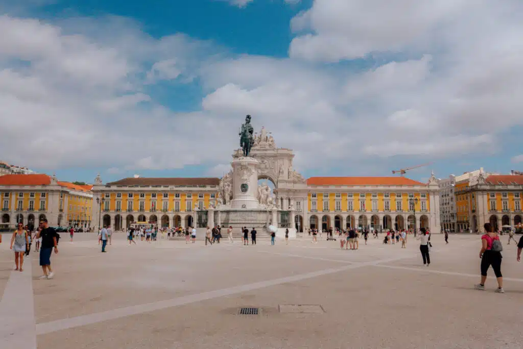 A highlight during 3 days in Lisbon, this large public square features people walking, a central equestrian statue, and a grand archway flanked by yellow buildings under a partly cloudy blue sky.