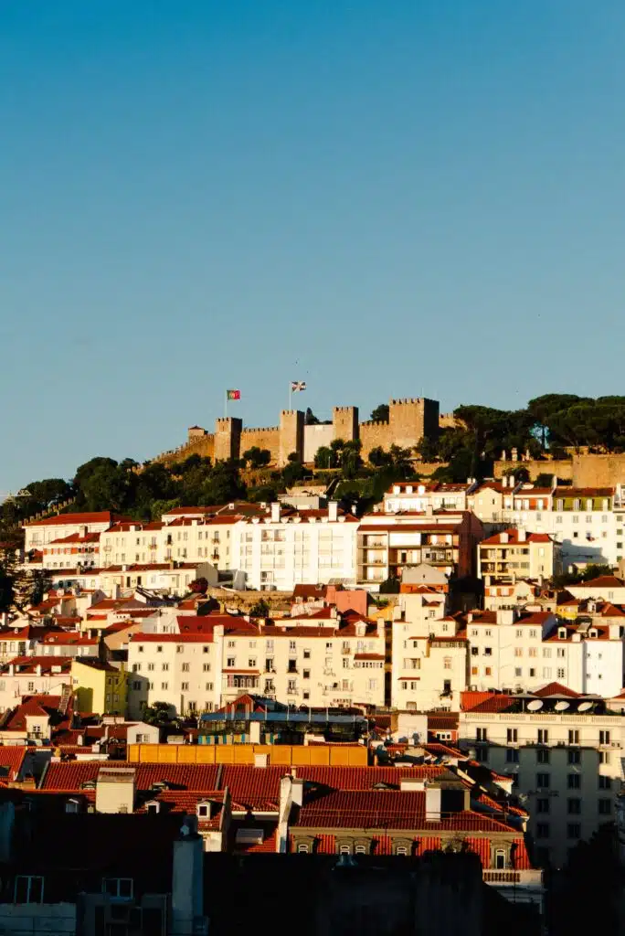 Enjoy a stunning view of Lisbon’s colorful hillside buildings with red-tiled roofs and historic São Jorge Castle—an unforgettable scene to experience during your 3 days in Lisbon under clear blue skies.