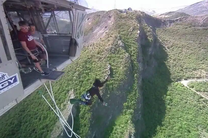 A person bungee jumps off a high platform over a lush green canyon, while two people watch from above. The stunning cliffs and distant mountains offer the perfect backdrop for one of the best first-time solo travel destinations.