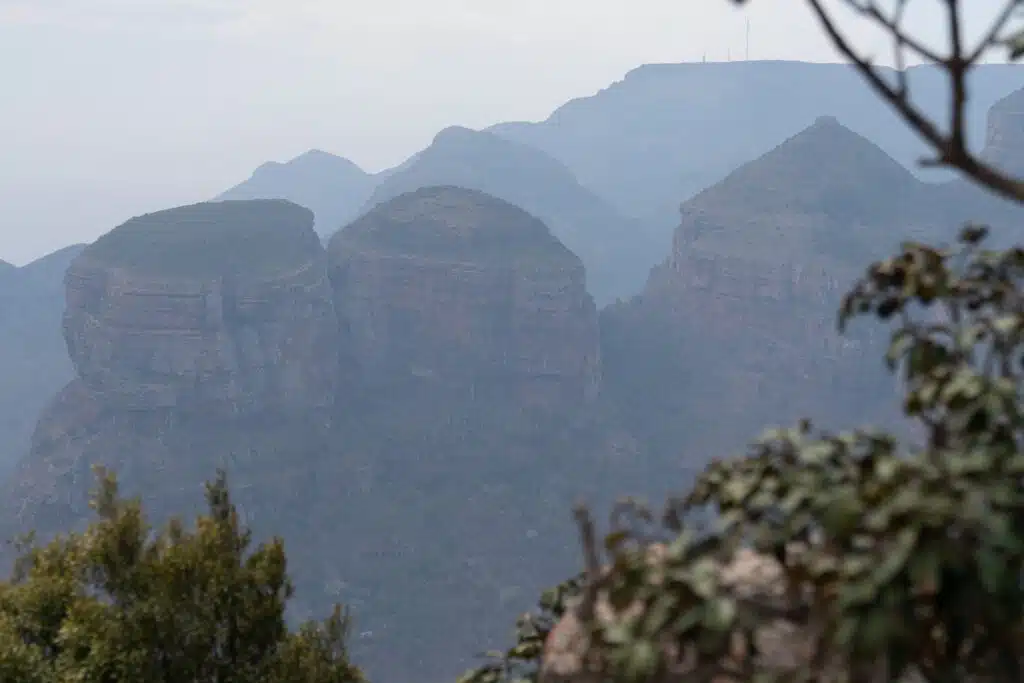 Misty mountain landscape with large, rounded rock formations and sparse vegetation in the foreground, partially obscuring the view—an ideal scene to encounter on adventurous African Overland Tours.