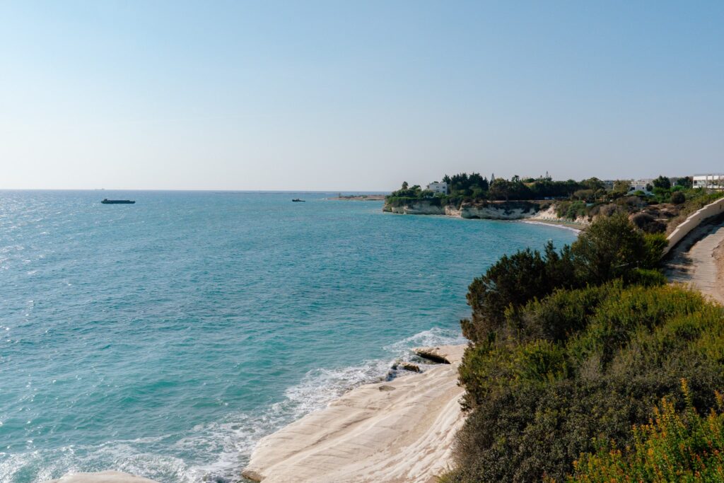 A scenic coastline with turquoise water, white rocky cliffs, and lush green vegetation under a clear blue sky. A house and other buildings are visible near the shore—an ideal spot to stay connected with the best eSIM for Europe.