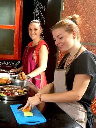 Three people are preparing food together in a kitchen, sharing smiles and fresh ingredients—just like friends exploring new flavors on a 1-week Kerala itinerary. Various vegetables and utensils are spread across the counter as they cook.