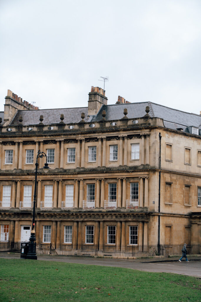 A historic Georgian-style building with tall windows and stone columns, perfect to admire during one day in Bath, sits beside a grassy area with a black street lamp and metal railings.