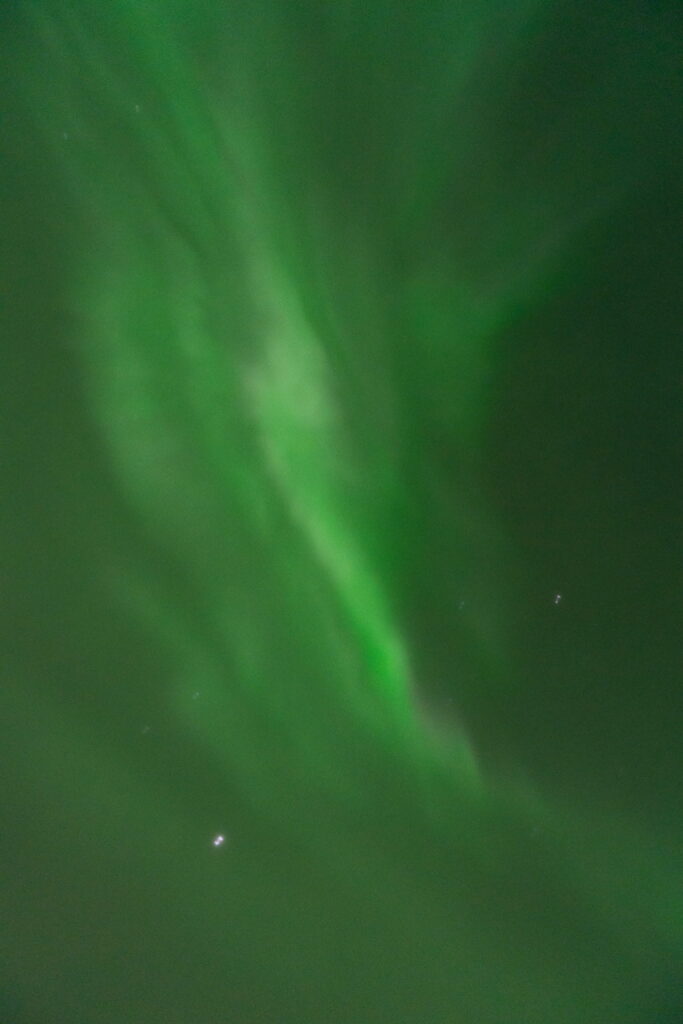 Green aurora borealis lights swirl across a dark night sky, dotted with stars—a magical highlight of any 3 Day Tromso Itinerary.