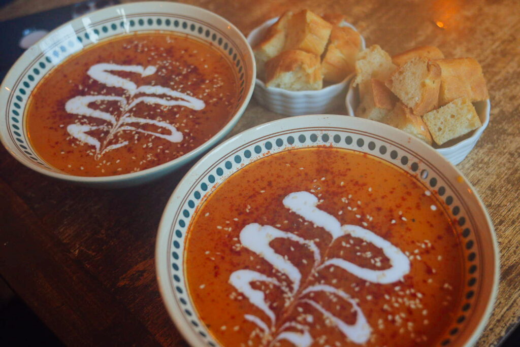 Two bowls of creamy tomato soup with white swirl designs on top, served with cubed bread on a wooden table—perfect comfort food to start your 3 Day Tromso Itinerary in Norway.