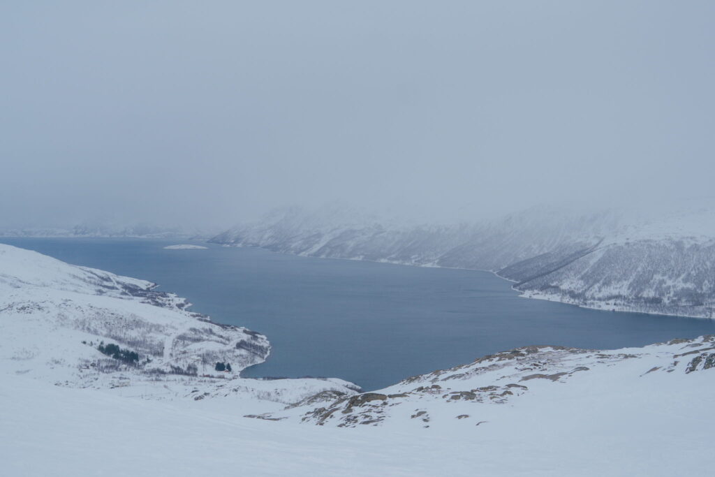 A wide river or fjord winds through a snow-covered, mountainous landscape under a cloudy sky, creating a tranquil winter scene—perfect inspiration for your 3 Day Tromso Itinerary.