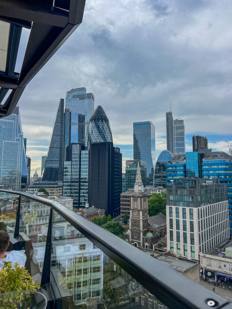 View of London’s modern skyline with distinctive skyscrapers like the Gherkin and the Leadenhall Building, seen from a rooftop terrace with glass railings—a perfect spot for visitors using sim local to stay connected as they take in the blend of old and new architecture.
